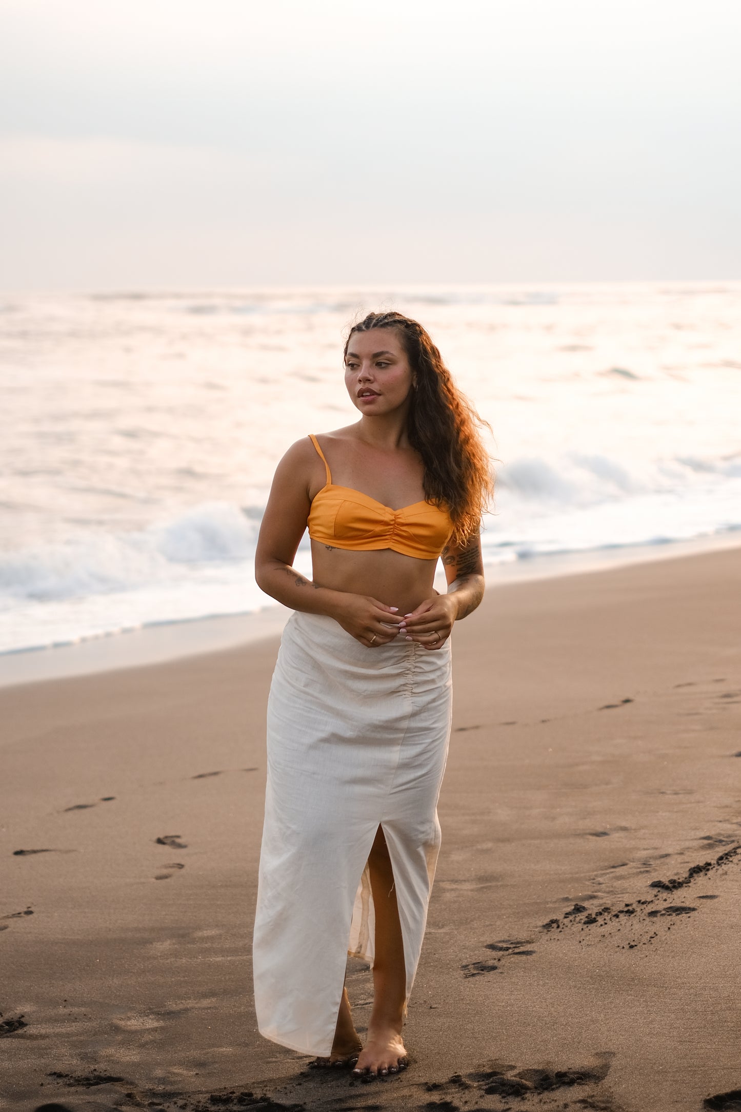 Femme portant une jupe longue jaune pâle avec une fente et un crop top orange. Collection printemps/été, mode éthique et féminine, fabriquée au Portugal avec des tissus dormants.