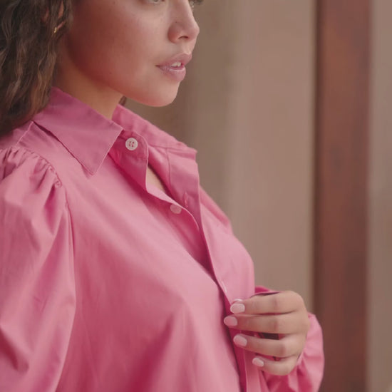 Femme portant une chemise oversize rose framboise avec des manches bouffantes. Collection printemps/été, mode éthique et féminine, fabriquée au Portugal avec des tissus dormants.